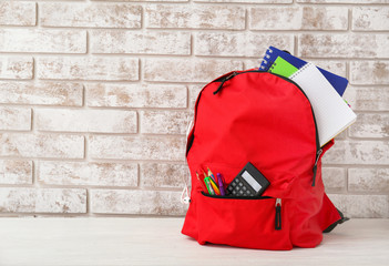 School backpack with stationery on table against brick wall