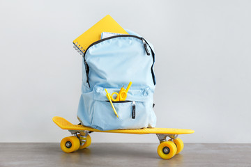 School backpack with stationery and skateboard on table against light background