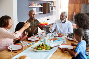 Multi-Generation Family Sitting Around Table At Home Enjoying Meal Together