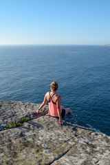 Morning view of a young female hiker sitting on a rock at North Head, a headland in Manly and part of Sydney Harbour National Park in Sydney, New South Wales, Australia.