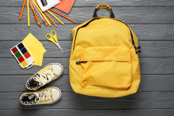 School backpack, shoes and stationery on wooden background