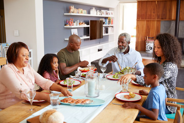 Multi-Generation Family Sitting Around Table At Home Enjoying Meal Together