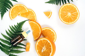 Natural cosmetic skincare serum packaging with leaf fern and fresh juicy orange fruit on white background. Beauty vitamin ingredient. alternative medicine. Flat lay, top view, copy space