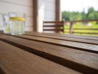 Garden furniture on the terrace of a country house, hotel. Two glasses with a refreshing drink with lemon in the distance, blurred, on a wooden table, focus on the tabletop. Space for text.