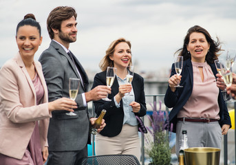 A group of joyful businesspeople having a party outdoors on roof terrace in city.