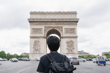 a man with backpack looking at Arc de Triomphe, famous landmark and travel destination in Paris,...