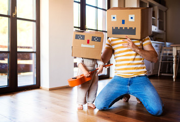 A toddler girl with father playing with cardboard monster indoors at home.