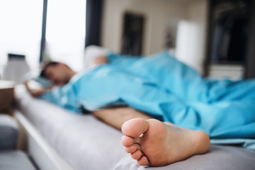 Young man sleeping in bed at home, close-up of bare foot.