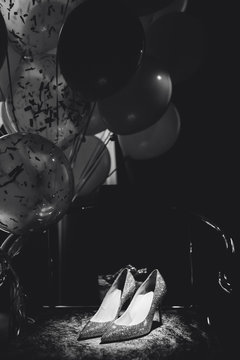 Bride Accessory Shoes on Chair and Balloons Photo. Classical Woman Stylish Sparkle Fancy Cool Footwear Decorated Bunch of Air Helium Bubbles. Beautiful Monochrome Black and White Image