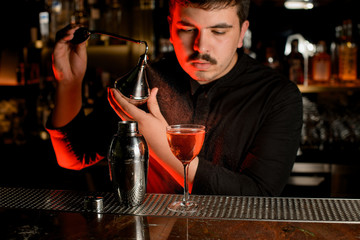 Professional male bartender spraying from the diffuser on the delicious cocktail in the glass