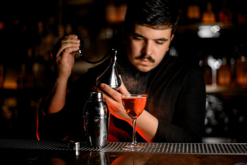 Professional male bartender spraying from the diffuser on the cocktail in the glass