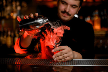 Bartender with mustaches pouring a smoke into the cocktail glass from the shaker
