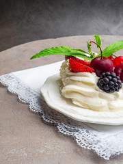 Rustic Pavlova cake with fresh strawberries, cherrys, blackberrys, mint and whipped cream over concrete background.