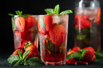 Fresh lemonade with ice, mint and strawberry on top in glass on black table background. Cold summer drink. Sparkling glasses with berry cocktail