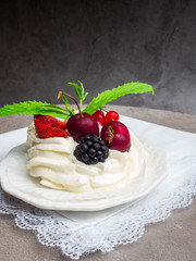Rustic Pavlova cake with fresh strawberries, cherrys, blackberrys, mint and whipped cream over concrete background.