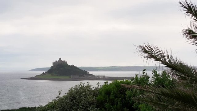 View from a terrace in Marazion of the english medieval castle and church of St Michael's Mount in Cornwall on a cloudy spring day.Zoom out 4k footage