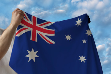 beautiful national flag of the country of Australia in male hands against the blue sky with clouds