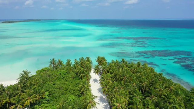aerial view of a small island in the Maldives with a white sand trail cutting the island in the middle. A gentle breeze is moving the pam tree leaves, no signs of human activity