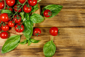 Fresh cherry tomatoes with green basil leaves on a wooden table. Top view