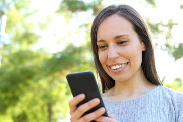 Happy woman checking smart phone message in a park