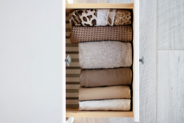 Fototapeta na wymiar extended drawer of white wooden chest with a row of neatly folded warm clothes of brown shades, top and side view