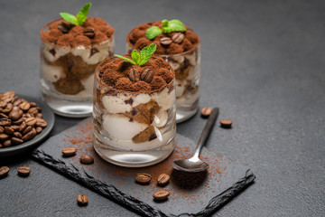 Classic tiramisu dessert in a glass on stone serving board on dark concrete background