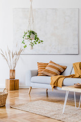 The modern boho compostion at living room interior with design gray sofa, wooden coffee table, rattan basket and elegant personal accessories. Honey yellow pillow and plaid. Cozy apartment. Home decor