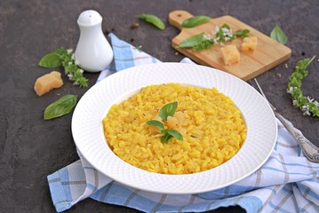 Saffron risotto in a white plate on a dark concrete background.
