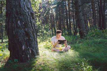 Man reading a book in a green summer forest.