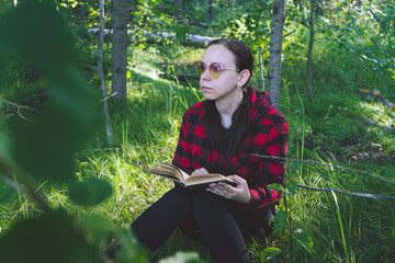Woman reading a book in a green summer forest.