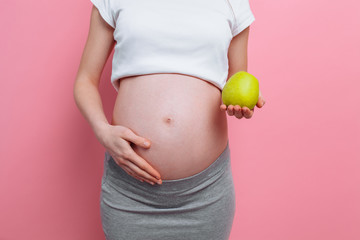 Pregnant woman holding a green apple near the belly. The concept of pregnancy, motherhood, proper nutrition