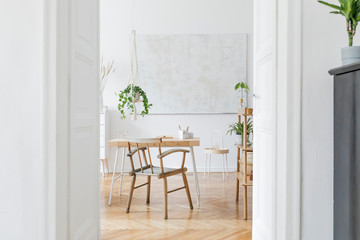 Stylish and boho home interior of living room with wooden desk, chair and shelf. Design and elegant accessories. Botany home decor with a lot of plants and plant stand. Abstract painting on the wall. 