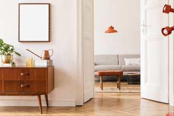 Stylish room of home interior with brown mock up frame, design sofa, furnitures, vintage cupboard with elegant accessories, plants and red retro lamp. Cozy home decor. Minimalistic concept.