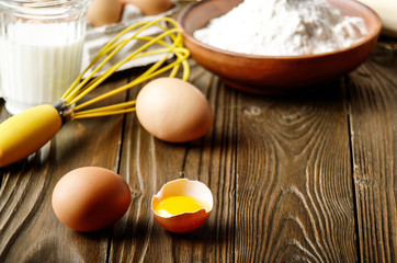 Raw organic brown chicken broken eggs with yolk flour milk and whisk on kitchen wooden table