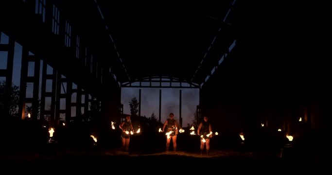 Four women in leather clothes with fire dance and show fire show a man with a flamethrower in the back plays with the flame in slow motion.