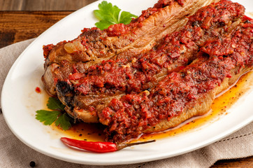 Grilled pork ribs in spicy sauce with tomatoes. Ketogenic and paleo food. Large portion on a white plate. Close up and horizontal orientation.