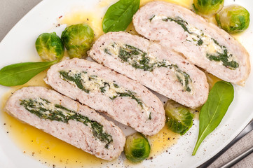 Stuffed chicken roll with cheese and spinach. A large portion with a side dish of Brussels sprouts and melted butter. Ketogenic and paleo food. Top view. Close up and horizontal orientation.