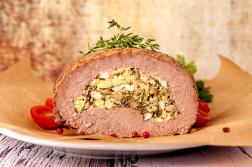 Meatloaf stuffed with eggs and fried onions. A large portion of meat is cut and served in a rustic style. .Close up and horizontal orientation.