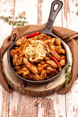 Fried pork with onions and hot pepper in a cast iron pan. Rustic decor. A large portion of meat. .Close up and vertical orientation.