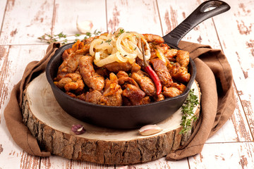 Fried pork with onions and hot pepper in a cast iron pan. Rustic decor. A large portion of meat....