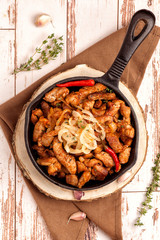 Fried pork with onions and hot pepper in a cast iron pan. Rustic decor. A large portion of meat. .Close up and vertical orientation.