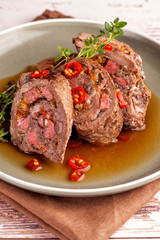 Beef tenderloin rolls stuffed. Slices of meat served on a plate in a sauce and with fresh vegetables and herbs. .Close up and vertical orientation.