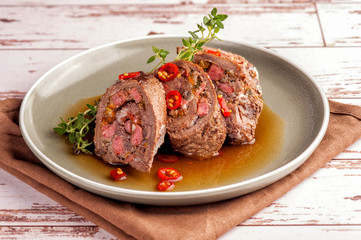 Beef tenderloin rolls stuffed. Slices of meat served on a plate in a sauce and with fresh vegetables and herbs. Close up and horizontal orientation.