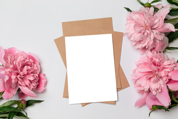 Mockup of horizontal business craft envelope with a sheet of white paper with bouquet of beautiful peonies on a gray background.