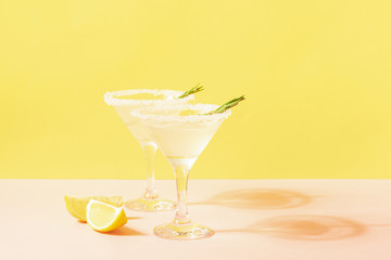 Lemon lemonade drink in elegant glasses on a bright pastel colored background. Bright sunshine. Summer concept.