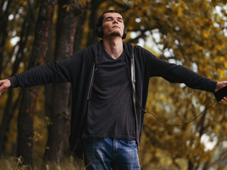 Obraz premium A young man in the autumn forest enjoys listening to music with headphones