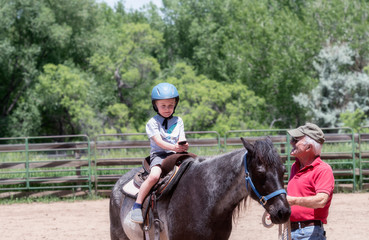 Toddler with a Safety Helmet on Goes on a Pony Ride at a Local Farm with his Horse Being Led by His...