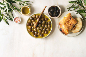 Variety of green and black whole olives in olive oil served in ceramic bowls with fresh baked...