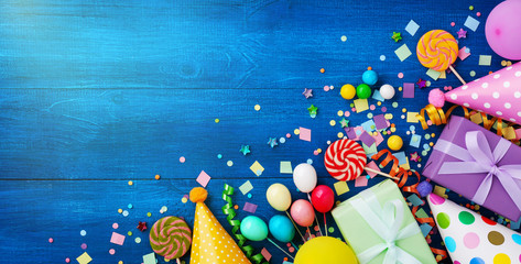 Holiday background with balloons, gift boxes and confetti. Birthday and party supplies on blue table top view. Banner format.