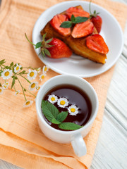 very tasty carrot cake decorated with strawberries on a white table and a Cup of fragrant flower tea